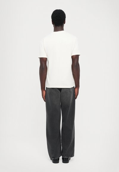 Λευκό βαμβακερό t-shirt με στρογγυλή λαιμόκοψη, συνδυασμένο με χαλαρά σκούρα γκρι τζιν παντελόνια; και τα δύο έχουν λεία υφή και απλό σχέδιο.