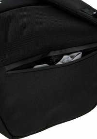 Bolsa de tela negra con un panel de malla texturizada y un bolsillo con cremallera que revela contenido gris. Superficie lisa y diseño minimalista.