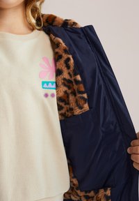 Chaqueta de piel sintética con estampado de leopardo y forro azul marino. Sudadera beige por debajo con coloridos diseños florales en rosa y azul.