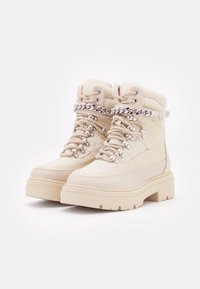 Bottes chelsea beige avec un dessus en cuir texturé, une semelle plateforme épaisse et un laçage à l'avant avec accents en métal argenté et détails en chaîne.