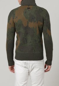 Grün-brauner Strickpullover mit hohem Kragen; verfügt über ein Tarnmuster, gerippte Bündchen und Bund; texturiertes, warmes Material.