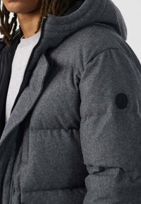 Giacca imbottita grigia in tessuto strutturato con cappuccio aderente, dotata di chiusura con zip e toppa rotonda con logo sulla manica.