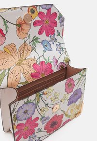 Bolso con estampado floral que presenta flores multicolores sobre un material blanco texturizado, con un interior marrón y un cierre redondo de botón dorado.