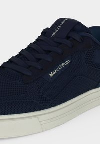 Baskets bleu marine Marc O’Polo en tissu texturé, lacets bleu marine et semelle en caoutchouc blanche, avec le nom de la marque sur la languette et le panneau latéral.