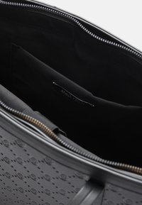 Interno di una borsa tote nera con texture, rivestito in tessuto liscio, dotato di chiusura a zip e un'etichetta che reca la scritta "ANNA FIELD."
