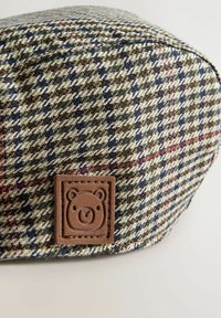 Villa-pipo, jossa on houndstooth-kuvio vihreänä, sinisenä ja kermanvärisenä, sisältää ruskean nahkalaatan, jossa on karhun kuvio. Pehmeä rakenne.