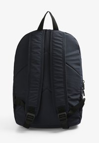 Mochila navy con correas acolchadas y un asa superior. Cuenta con un cierre de cremallera, costuras reforzadas y correas laterales ajustables. Textura suave.