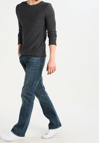 Dunkelgraues Langarmshirt kombiniert mit verblassten blauen Jeans und weißen Turnschuhen. Das Shirt hat einen Rundhalsausschnitt und einen strukturierten Stoff.