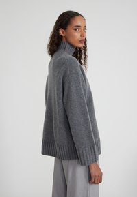 Pull en tricot gris surdimensionné avec un col roulé haut, des poignets et un ourlet côtelés. La texture douce et la coupe décontractée améliorent le confort.