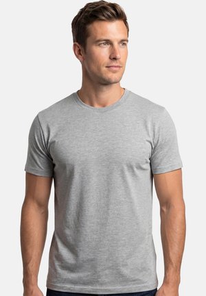 Man with short brown hair wearing a plain light gray short-sleeve crew neck t-shirt, looking slightly to the right.