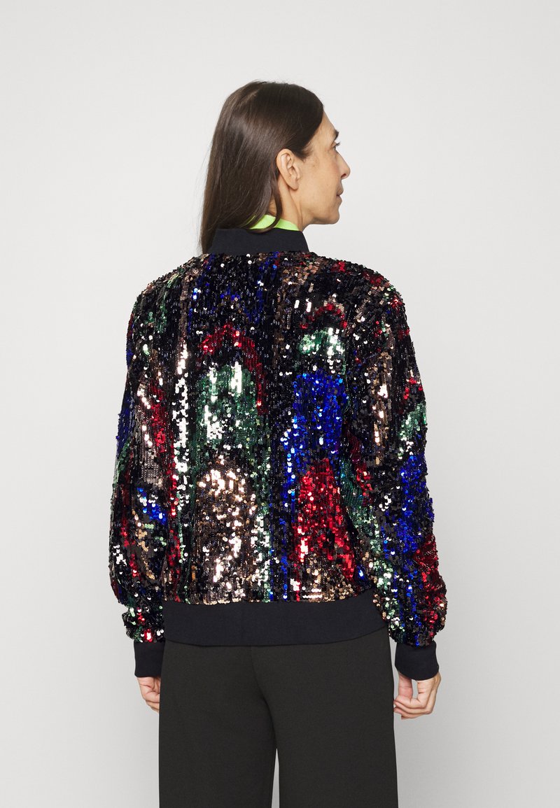 Veste bomber en sequins avec un motif multicolore rouge, vert, bleu et noir. Poignets et col en tricot noir. Texture lisse.