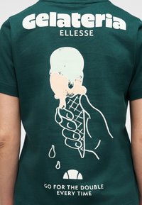 Εικονογράφηση χεριού που κρατάει έναν παγωμένο κώνο παγωτού που λιώνει σε σκούρο πράσινο πουκάμισο με το κείμενο «gelateria ELLESSE» και «ΔΙΑΛΕΞΕ ΤΟ ΔΙΠΛΟ, ΠΑΝΤΑ.»