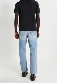 Svart bomullströja, ljusblå denimjeans med en blekt look, och svarta läderkängor, sedd bakifrån.