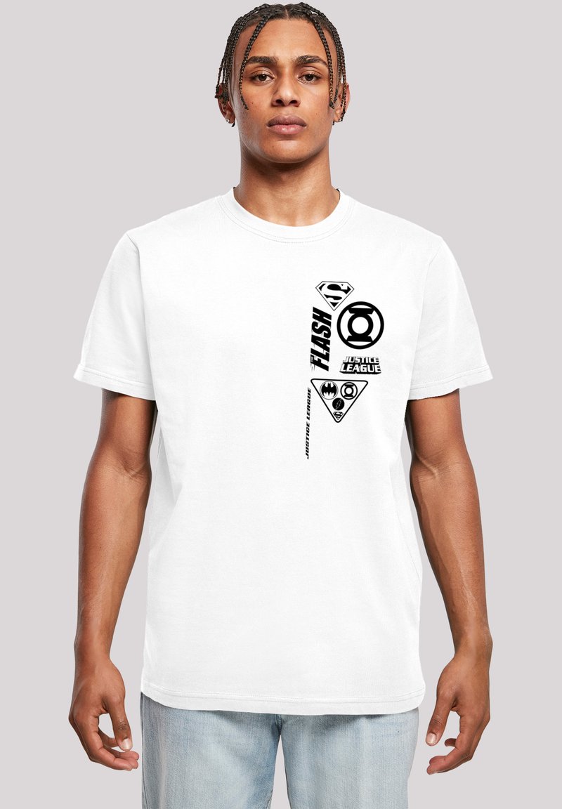 Vit bomullströja med svarta tryckta logotyper och text, inklusive superhjälte-symboler och namn, ordnade vertikalt på ena sidan.