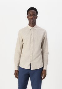 Camisa de botón de manga larga color beige claro con cuello, tejido texturizado y dobladillo recto, combinada con pantalones azul marino.