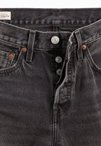 Jeans de mezclilla gris con cierre de botones, botones metálicos y remaches de cobre. Presentan una textura desgastada y un diseño clásico de cinco bolsillos.