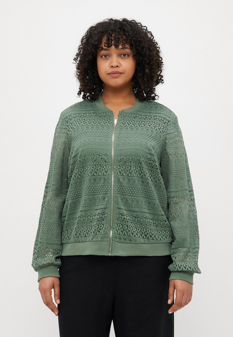 Veste bomber en dentelle vert clair avec fermeture éclair. Présente des motifs complexes, des poignets et un ourlet côtelés. Tissu léger et respirant.