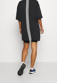 Camisa negra de corte oversize con un diseño en la parte posterior que presenta tres rayas verticales blancas, combinada con pantalones cortos negros y zapatillas deportivas.