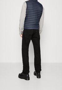 Navy puffer vest over gray sweatshirt, paired with black jeans and black chunky boots. Features a smooth texture and a fitted silhouette.