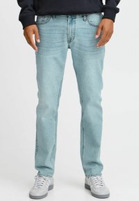 Jeans de mezclilla azul claro con un diseño de pierna recta, estilo de cinco bolsillos y una textura desgastada. Combinados con zapatillas blancas.