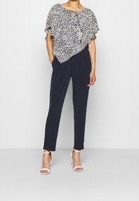 Haut léger à motifs avec une coupe décontractée, associé à un pantalon slim noir. Il présente un col rond et des sandales à talons blancs.
