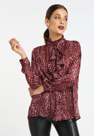 Blusa trasparente e volant in un vivace rosa con stampa leopardata nera, caratterizzata da un collo alto e dettagli con bottoni sui polsini.