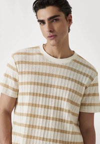 Gestreept brei shirt in crème en beige. Beschikt over een geribbelde textuur, korte mouwen en een ronde halslijn. Lichtgewicht en ademend materiaal.