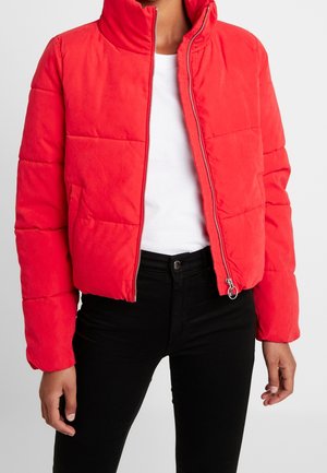 Rode gewatteerde donsjas met rits aan de voorkant, gedragen over een wit shirt en zwarte broek, zichtbaar van halverwege de borst tot de heupen.