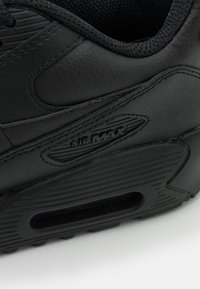 Fekete bőrsneaker, textúrázott dizájnnal, kiemelkedő Air Max márkázással és látható légbetéttel a talpában.