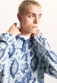 Ljusblå mönstrad skjorta med lång ärm och blåaktiga accenter, knappad krage och abstrakta mönster, med en mjuk textur och avslappnad passform.