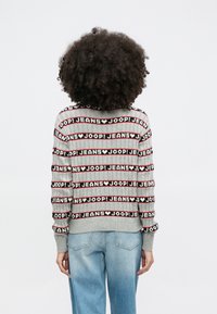 Γκρι πλεκτό πουλόβερ με έντονα μαύρα και κόκκινα γράμματα "JOOP! JEANS" σε ριγέ μοτίβο, με ριμπ τελείωμα και μανσέτες. Φορεμένο με ανοιχτόχρωμο μπλε τζιν.