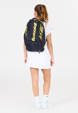 Sort og gul Babolat Aero rygsæk med justerbare stropper, flere rum og et slankt design, båret på ryggen af en person.