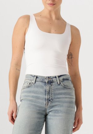 White fitted tank top with a square neckline, paired with light blue high-waisted jeans, featuring a slight fade and classic five-pocket design.