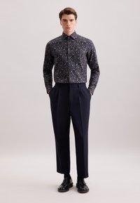 Pantaloni navy con una vestibilità tailored, abbinati a una camicia scura con un motivo astratto colorato. Tessuto morbido e design del colletto classico.