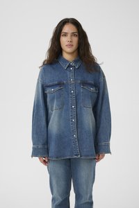 Camicia di jeans blu oversize con colletto a punta, bottoni frontali, due tasche sul petto e una trama sbiadita, abbinata a pantaloni in jeans coordinati.