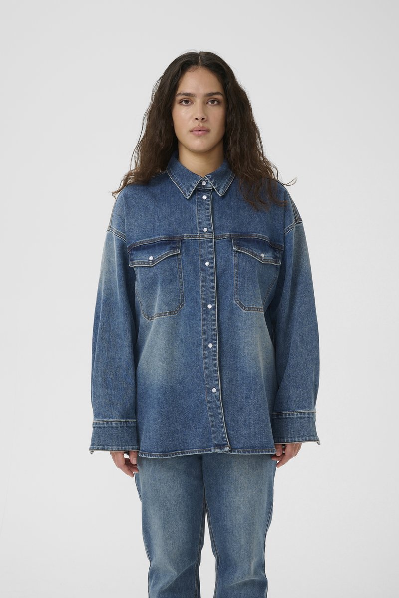 Camicia di jeans blu oversize con colletto a punta, bottoni frontali, due tasche sul petto e una trama sbiadita, abbinata a pantaloni in jeans coordinati.