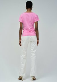 Camiseta rosa de manga corta hecha de tela suave, combinada con pantalones blancos de pierna ancha. Los pantalones tienen bolsillos traseros y una textura lisa.