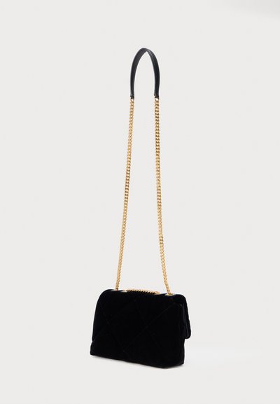 Mala de mão em veludo preto com design acolchoado, apresentando uma alça de corrente dourada e pega em couro preto. Forma compacta e estruturada.