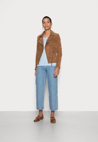 Brun ruskinds motorcykeljakke med skrå lynlås, lyseblåt t-shirt, afslappede blå jeans og brune loafers. Minimalistisk, struktureret design.