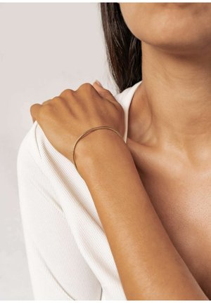 Gold bangle bracelet on a wrist, featuring a smooth, sleek design. The background is neutral, emphasizing the bracelet's details.