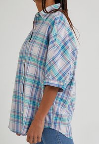 Camicia a maniche corte a quadri con tonalità blu, verde e viola, con bottoni e maniche arrotolate, realizzata in tessuto leggero.