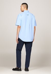 Light blue short-sleeve shirt with a straight hem and back logo detail, paired with dark navy slim-fit pants and black shoes.