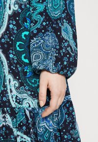 Blue and green paisley-patterned dress with a navy background. Features long puffed sleeves and a ruffled hem, made from lightweight fabric.