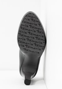 Chaussure à talon noire, inclinée pour montrer la semelle avec le motif "tamaris" et la taille 37 indiquée près du talon.