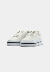 Weiße Wildleder-Sneaker mit dicker Sohle, einem schwarzen Akzentstreifen, perforierter Zehenbox und flachen Schnürsenkeln. Abgerundete Form und minimalistisches Design.