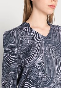 Blusa de padrão escuro com um design ondulado e marmorizado em preto e lavanda, com decote em V e ombros levemente bufantes.