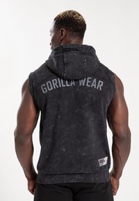 Zwarte mouwloze hoodie met een versleten textuur. "GORILLA WEAR" in het grijs op de achterkant gedrukt. Voorzien van een capuchon en een geribde zoom.