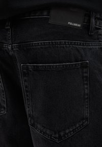 Čierne denimové džínsy so zadným vreckom, jemnou textúrou a obdĺžnikovou značkovou nálepkou s nápisom "PULL&BEAR."