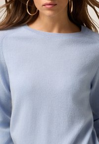 Jasnoniebieski sweter z dzianiny, okrągłym dekoltem i długimi rękawami, charakteryzujący się miękką teksturą i bezszwowym wykończeniem ramion.