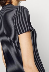 Tmavě modré pruhované tričko z měkké bavlny. Krátké rukávy, kulatý výstřih a úzký střih s tenkými bílými vodorovnými pruhy.